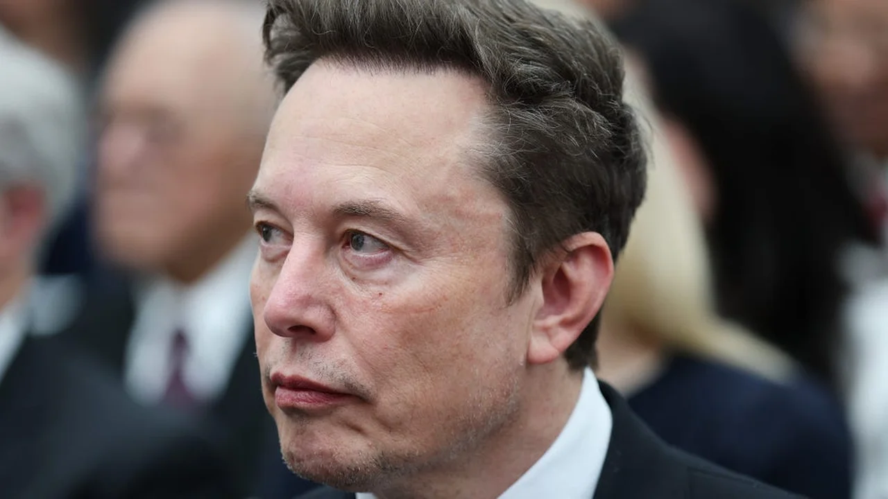 Close-up photo of Elon Musk in a dark suit and white shirt, looking slightly to the left