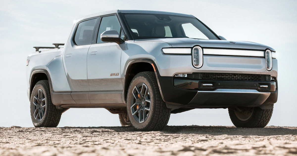 Silver Rivian R1T electric pickup truck parked on sandy outdoor terrain facing three-quarter front