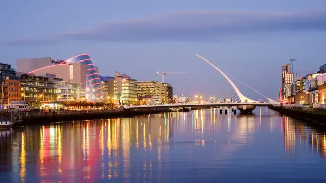 Dublin's River Liffey at dusk, with the harp-shaped Samuel Beckett Bridge and lit-up waterfront buildings