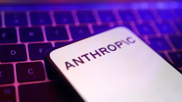 A phone showing the Anthropic wordmark lying on a laptop keyboard lit in purple