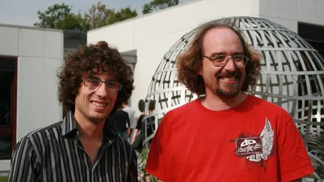 Two men smiling outdoors in front of a large metal globe sculpture
