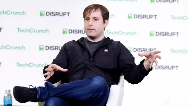 A man speaking on stage at TechCrunch Disrupt in front of a logo backdrop