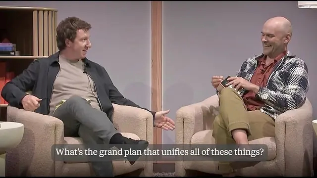 Two men talking in armchairs on a set, with a caption: 'What's the grand plan that unifies all of these things?'